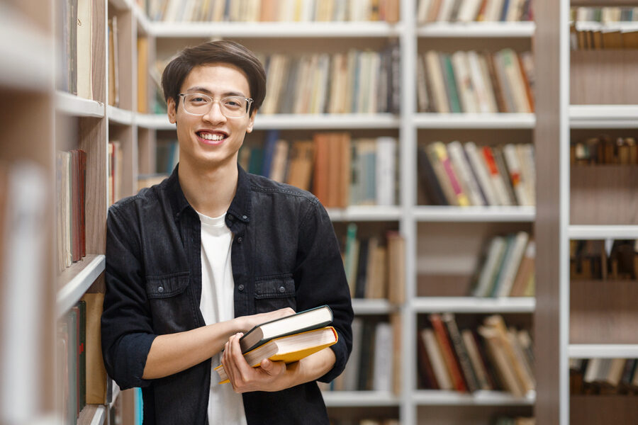 Smiling korean guy holding textbooks at library